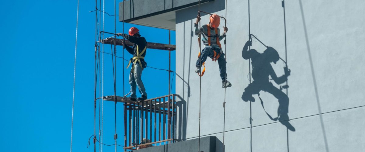 A couple of workers fixing and climbing a scaffolding while following all the safety measures