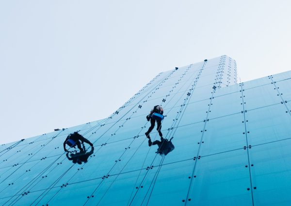 A vertical low angle shot of two people climbing a tall glass building during the day time